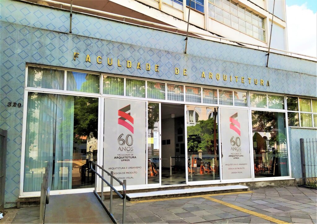 Image of the front of a blue building, written in gold letters "Faculdade de Arquitetura" (Rchitecture College) and glass doors.