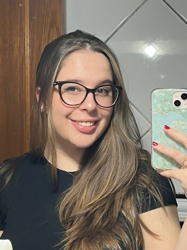A blonde girl smiling and holding her phone in front of the mirror.